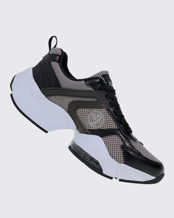 Right side view of the shoe, with black laces, grey mesh behind layered black overlays, a silver Zumbito logo, and a chunky white sole that dips under the arch.