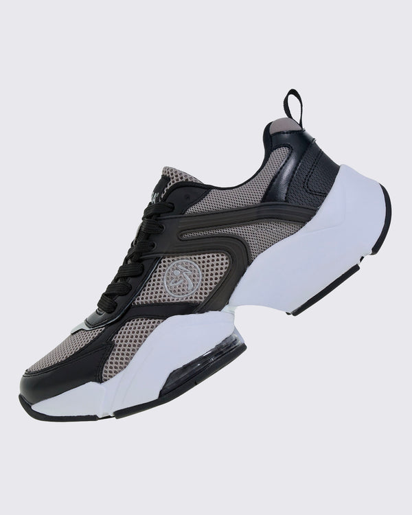 Left side view of the shoe, highlighting wavy black overlays across the grey mesh, a silver Zumbito logo, a black heel pull loop, and a clear air cushion under the forefoot.