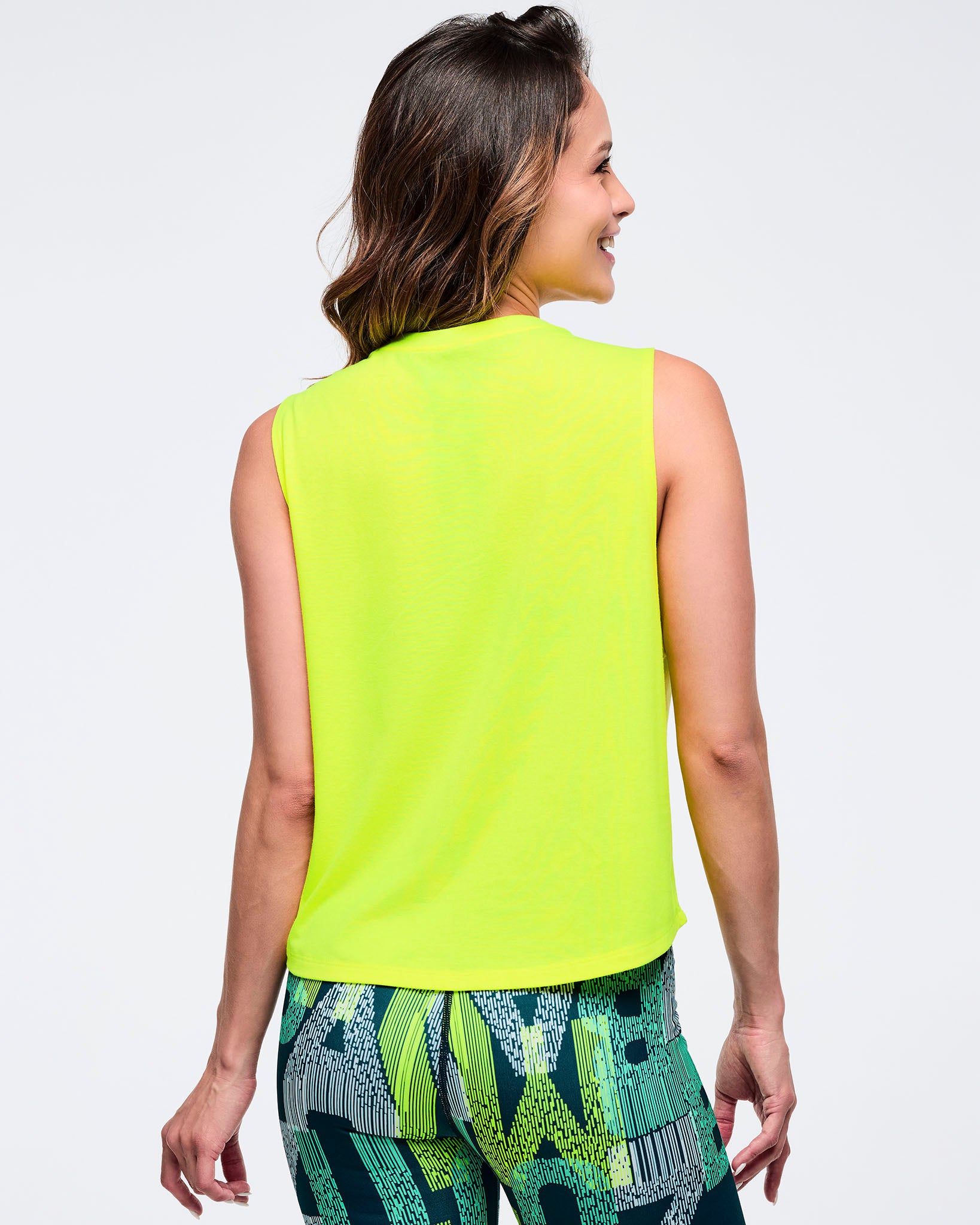 Back view of a neon yellow sleeveless tank on a female model, paired with green-and-black abstract print biker shorts, photographed on a white background.