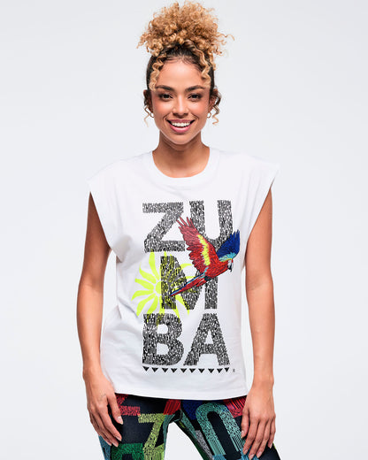 White sleeveless muscle tee with large “ZUMBA” text graphic and a colorful parrot and palm print on the front, worn by a female model with multicolor patterned leggings.