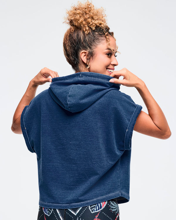 Back view of a navy denim short-sleeve hooded sweatshirt on a female model, shown with dark tropical-print leggings on a white background.