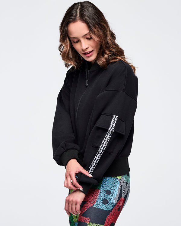 Black zip-up jacket featuring a sleeve cargo pocket and black-and-white wavy trim detail; female model wears multicolor letter-print leggings on a white background.