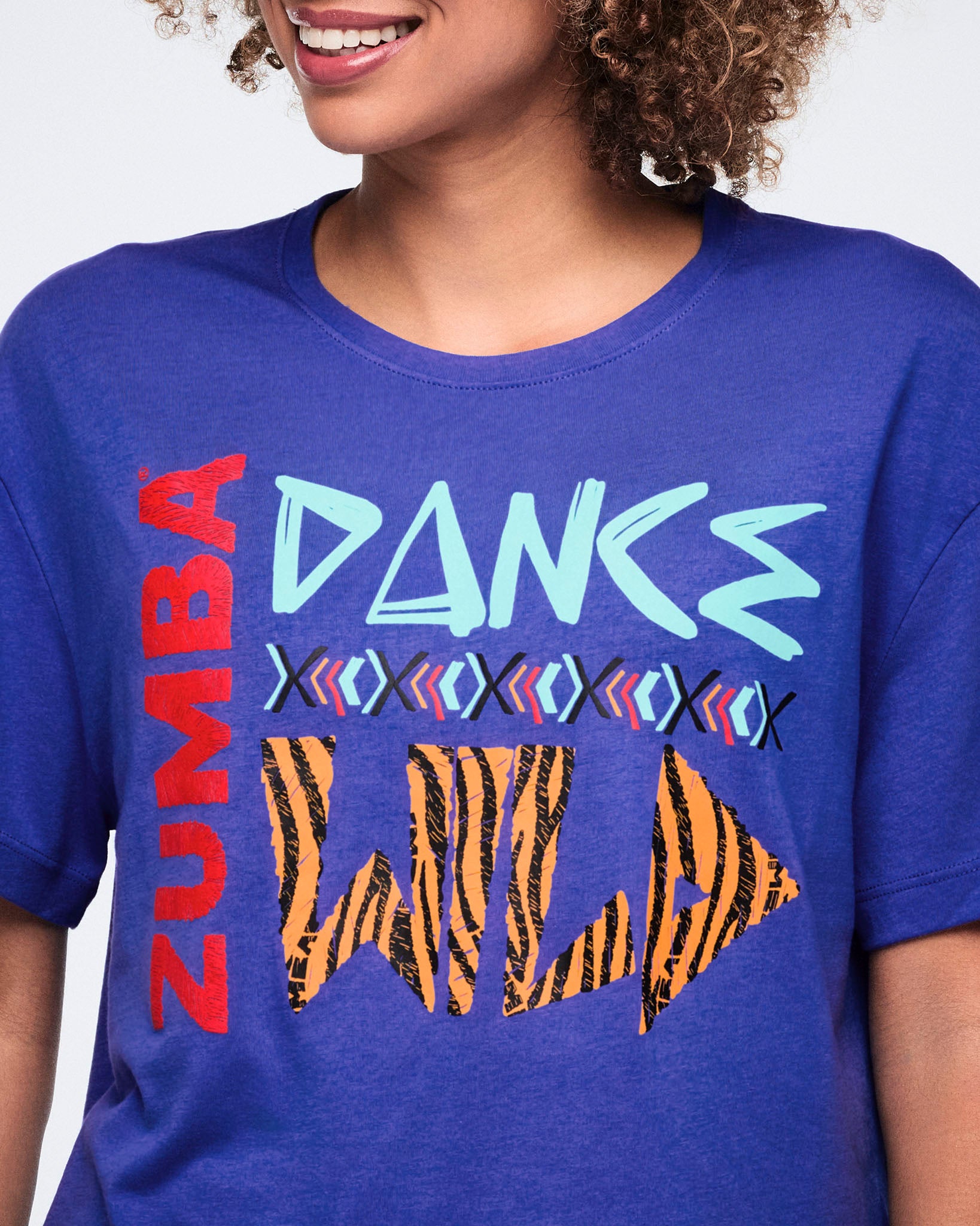 Close-up of the blue Zumba graphic T-shirt, highlighting the crew neckline and bold front graphic with red “ZUMBA,” light blue “DANCE,” and orange-and-black “WILD” lettering.