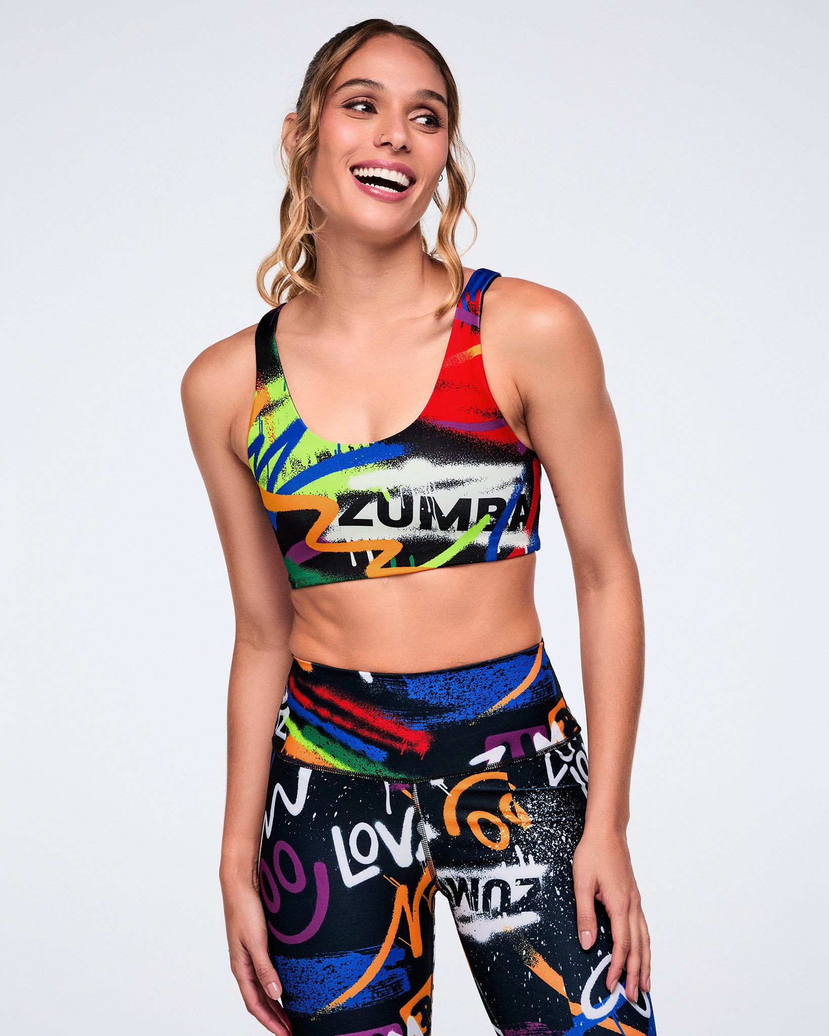 Female model wearing a colorful Zumba sports bra and leggings on a white background.