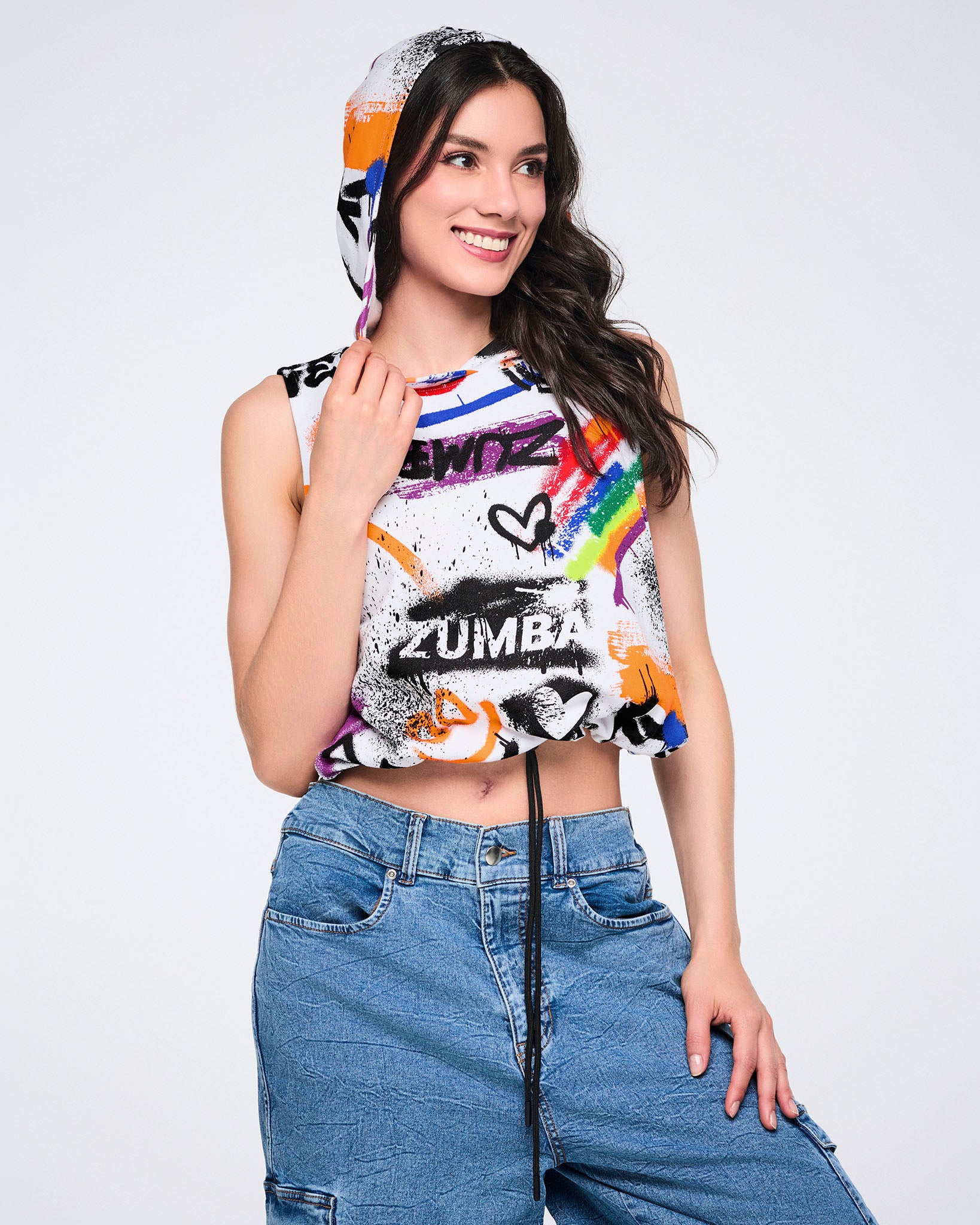 Female wearing a colorful Zumba sleeveless hoodie and denim cargo pants, against a white background.