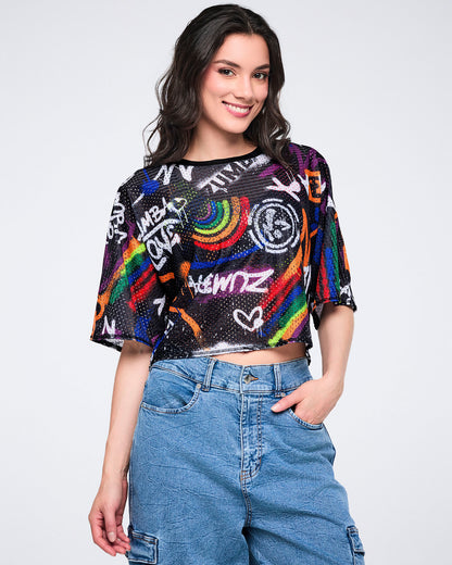 Female model wearing a colorful mesh graphic crop top and denim cargo pants on a white background.