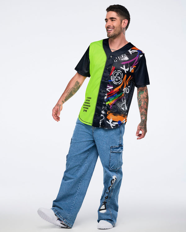 Male model in neon‑green and black graphic Zumba jersey and denim cargo pants standing against a white background.