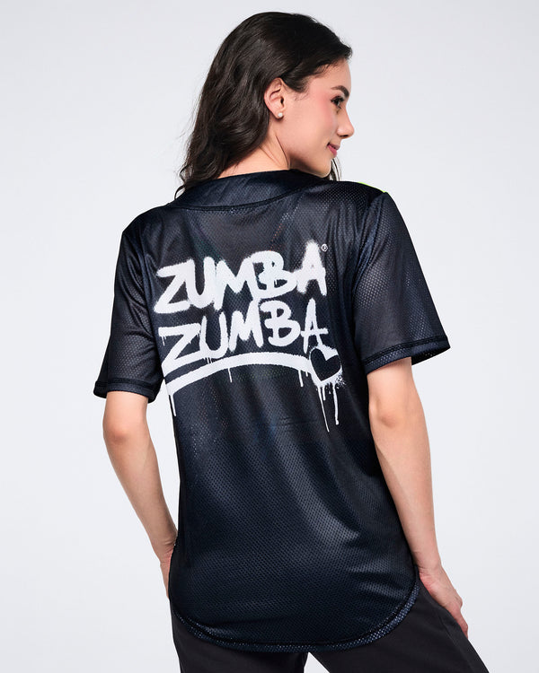 Female model showing the back of a black mesh Zumba jersey with white “Zumba Zumba” graffiti text with a heart on a white background.