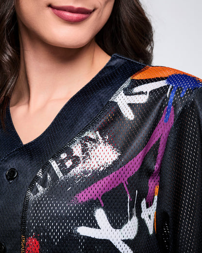 Close up detail of a female model wearing a black mesh Zumba jersey with bold multicolor graphics on a white background.