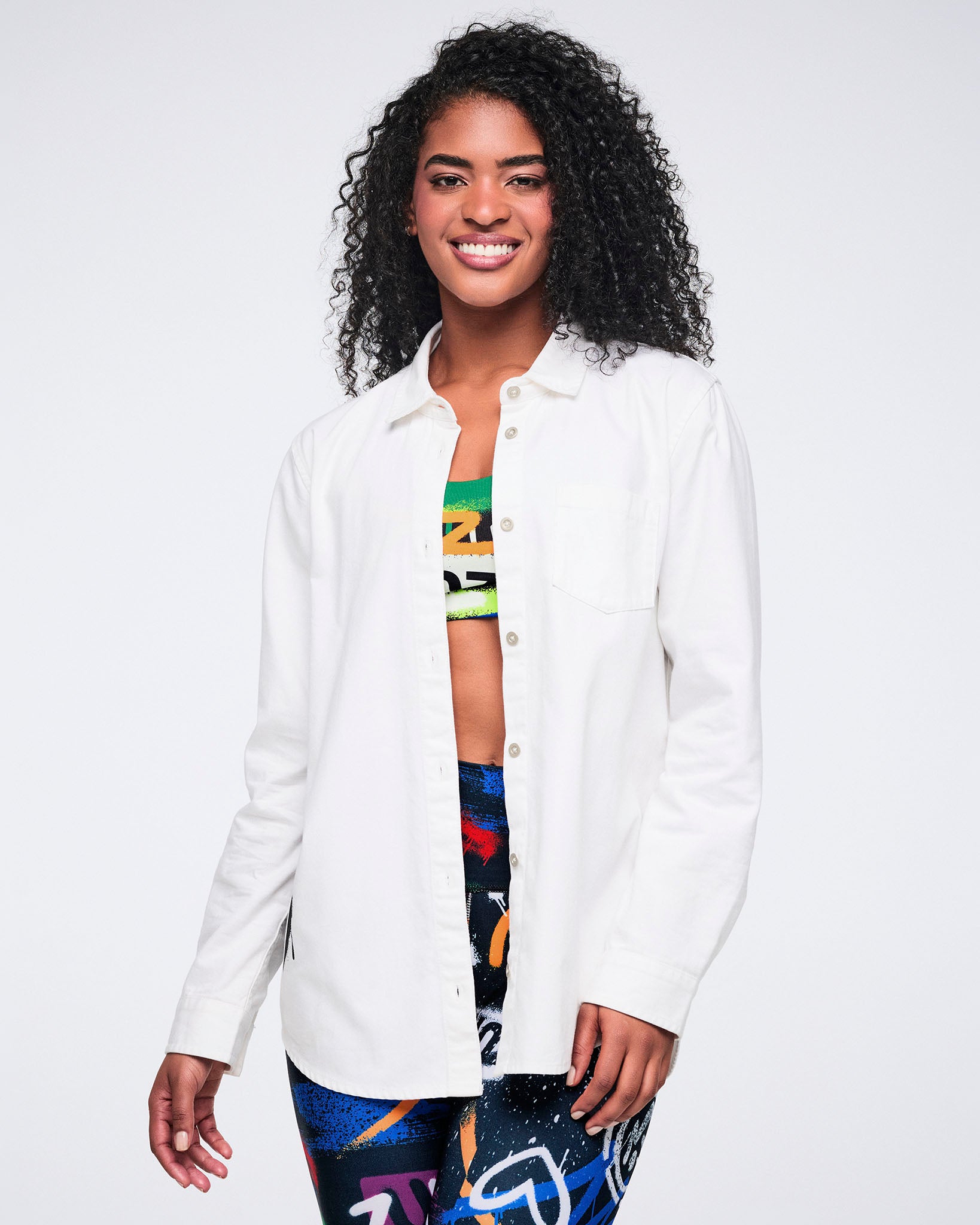 Female model wearing a white button down over a colorful bra and matching leggings on a white background.