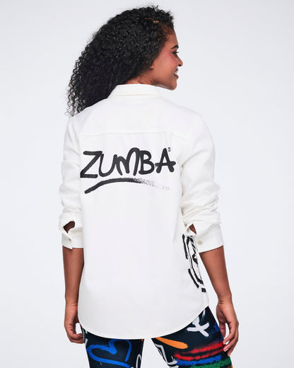 Female model showing the back of a white button down shirt with 'ZUMBA' towards the top, paired with colorful leggings against a white background.