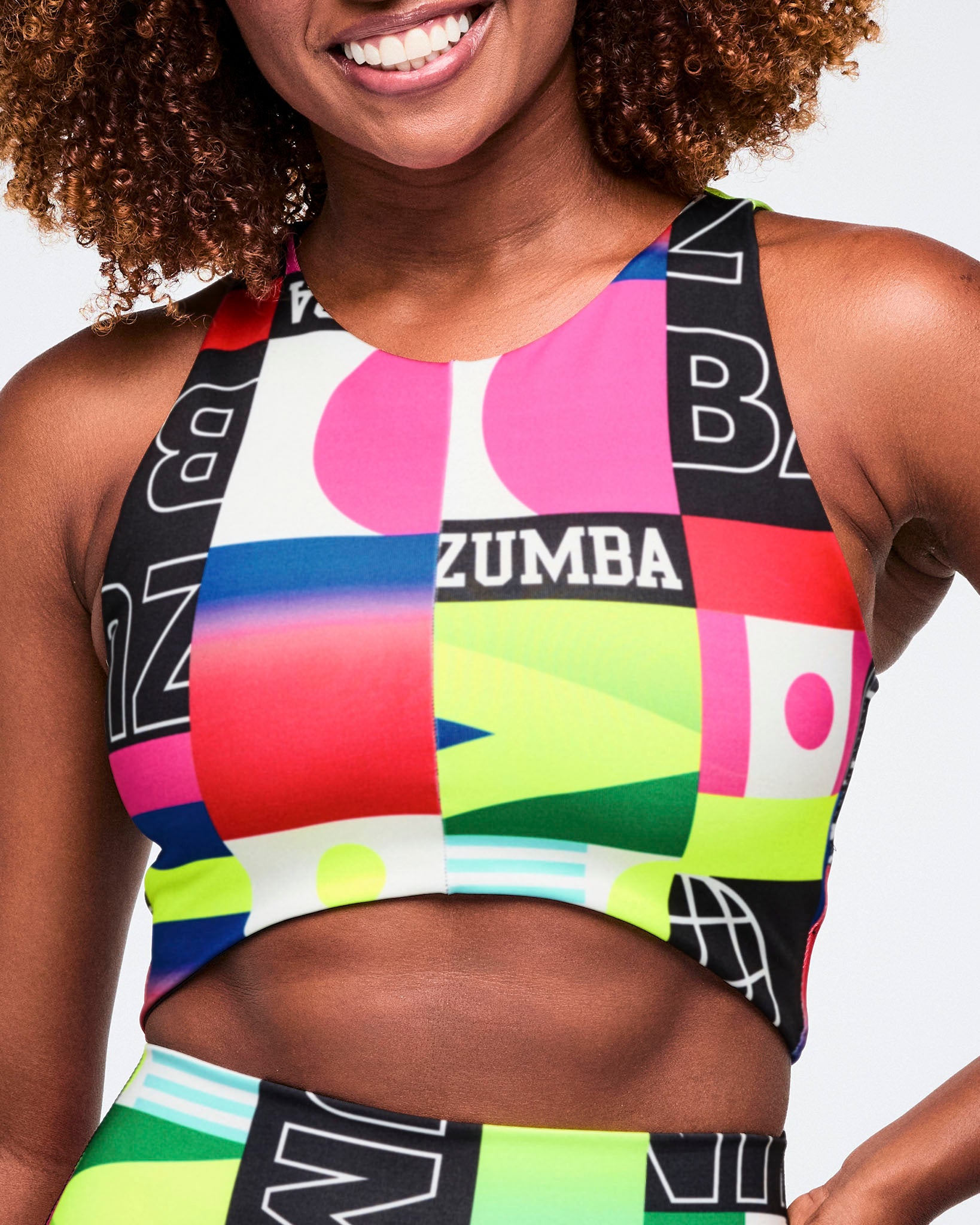 Female model wearing a colorful Zumba crop top with geometric patterns.