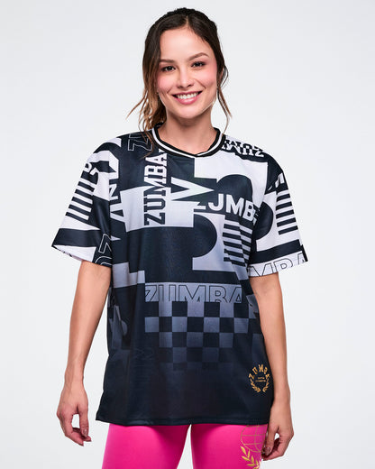 Female model wearing a Zumba branded black and white patterned shirt on a white background.