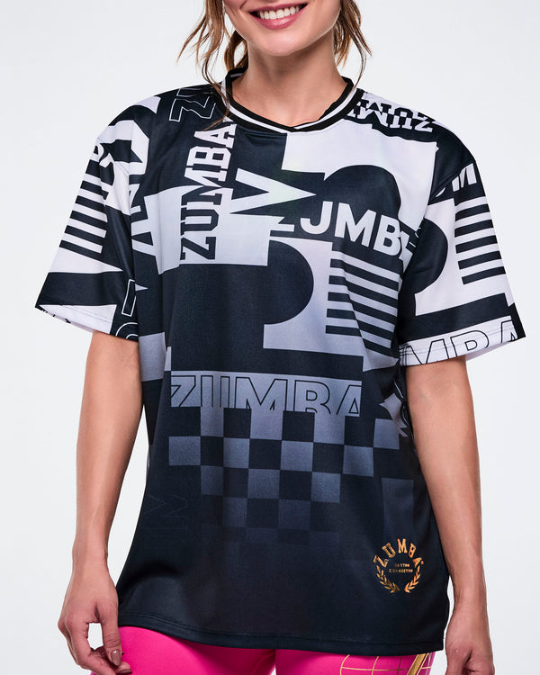 Close up of a female model wearing a black and white Zumba shirt with various patterns on a white background.