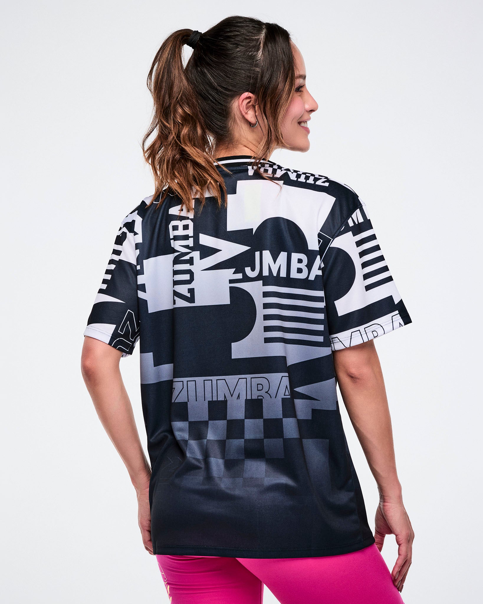 Back view of a female model wearing a Zumba branded black and white patterned shirt on a white background.