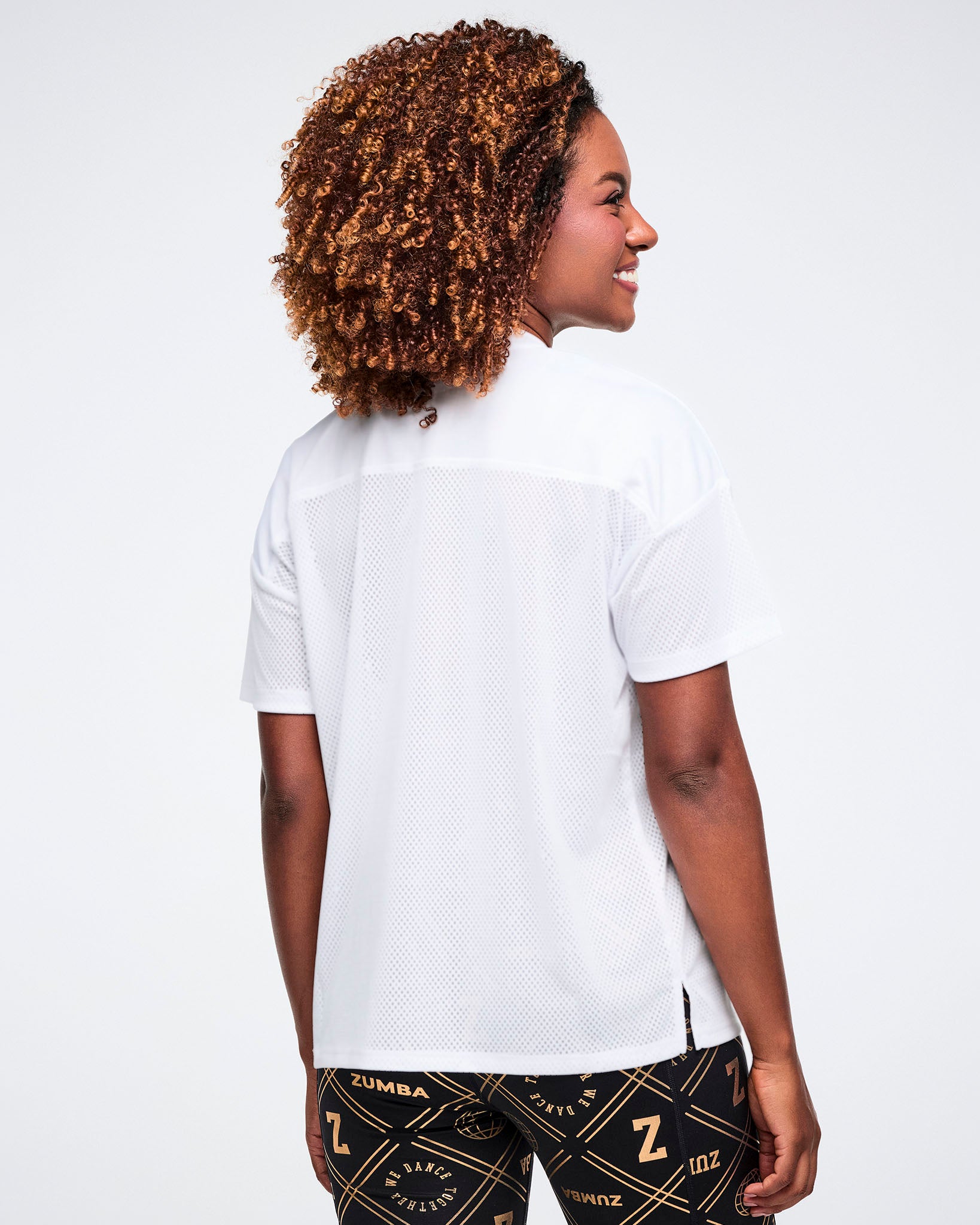 Female model, shown from the back wearing a white top and patterned black and gold leggings on a white background.