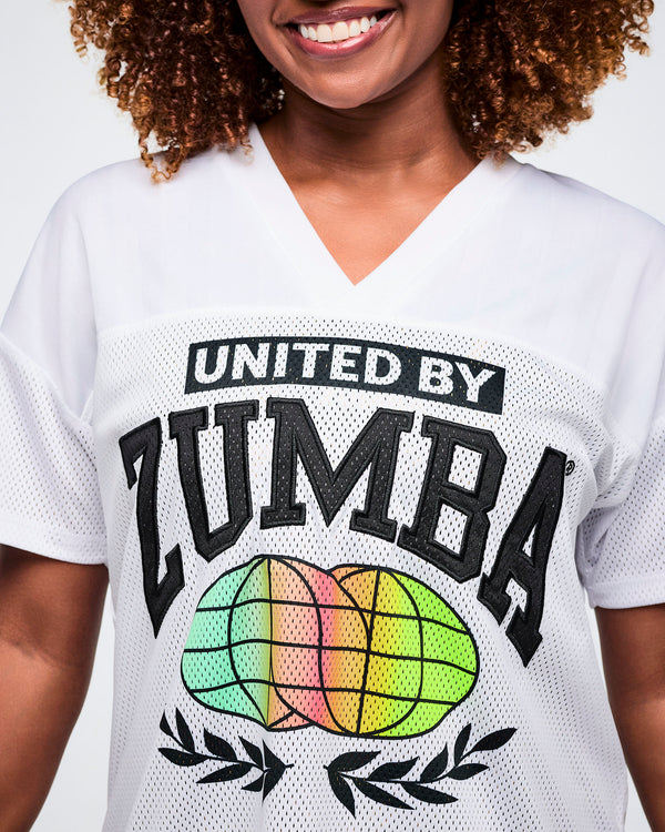 Close up of a female model wearing a white 'United by Zumba' top with a colorful globe design.