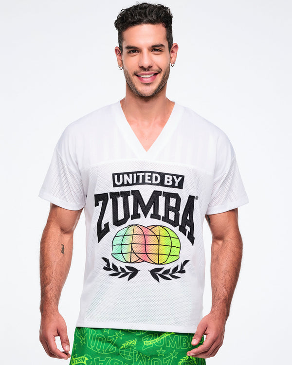 Male model wearing a white 'United by Zumba' top with colorful graphics on a white background.
