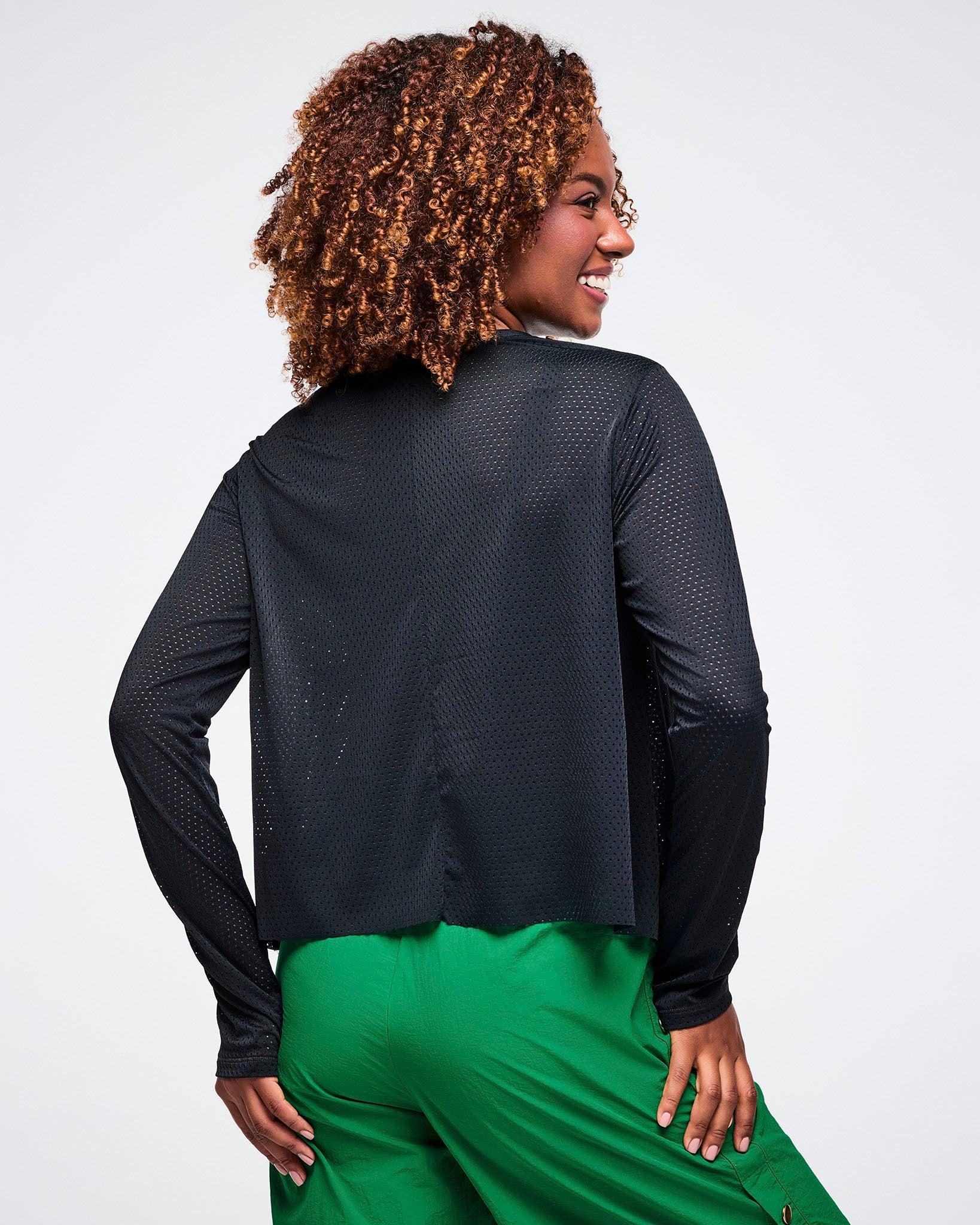 Back view of a female model wearing a black long-sleeve mesh top and green pants on a white background.