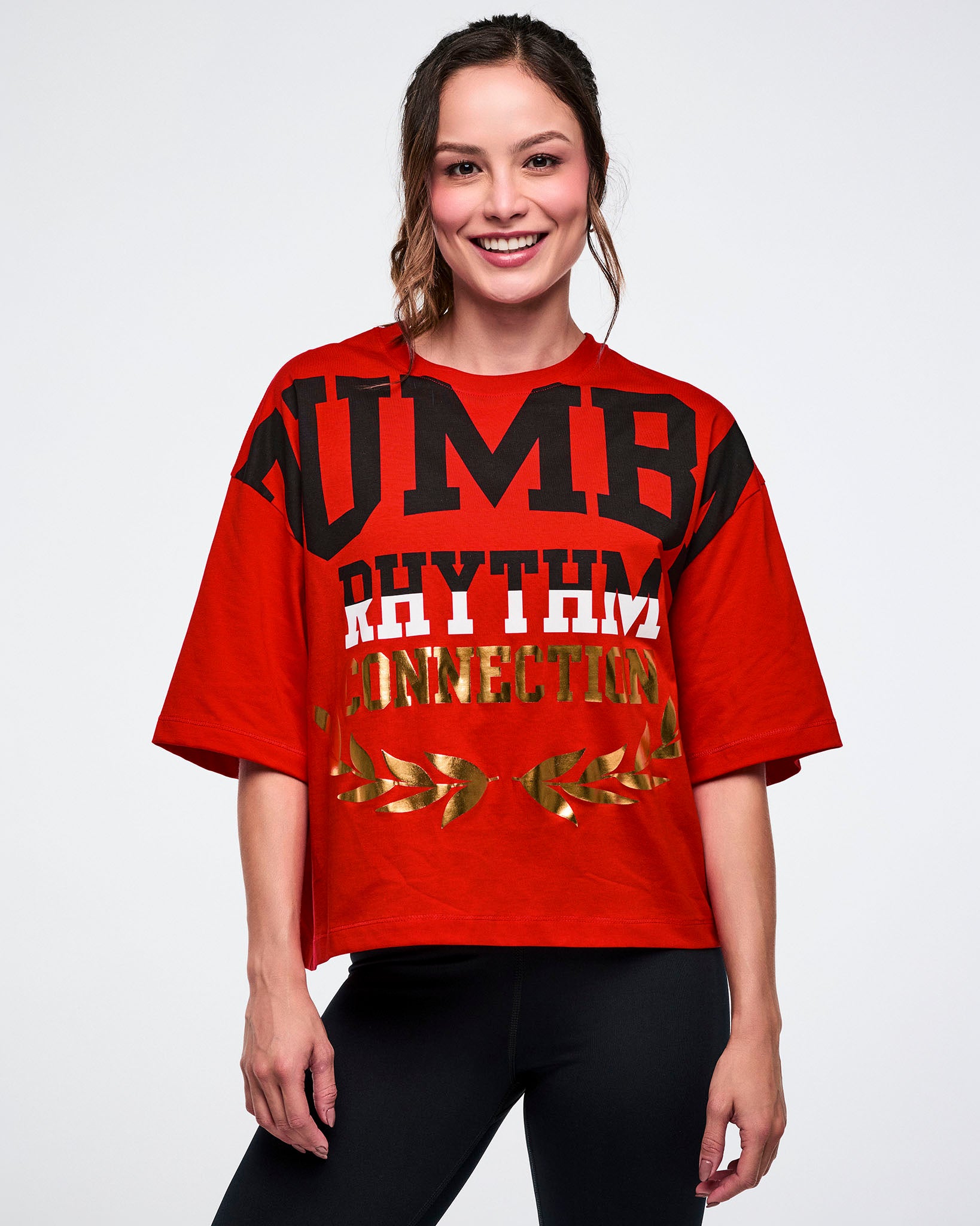 Female model in a red tee with bold black-and-white “ZUMBA Rhythm” and gold foil “Connection” text on a white background.