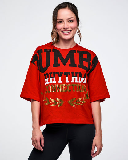 Female model in a red tee with bold black-and-white “ZUMBA Rhythm” and gold foil “Connection” text on a white background.
