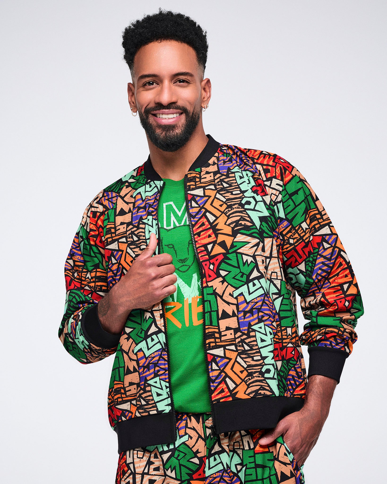 Multicolor Zumba print jacket with a zip front, black ribbed collar, cuffs, and hem. Male model wears the jacket over a green graphic T-shirt with matching print pants.