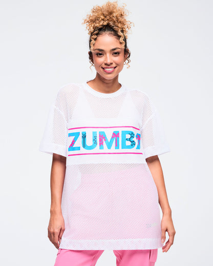White oversized mesh short-sleeve crewneck top with a wide chest panel featuring a bold “ZUMBA” logo in turquoise with hot-pink accents; shown on a female model wearing pink pants.