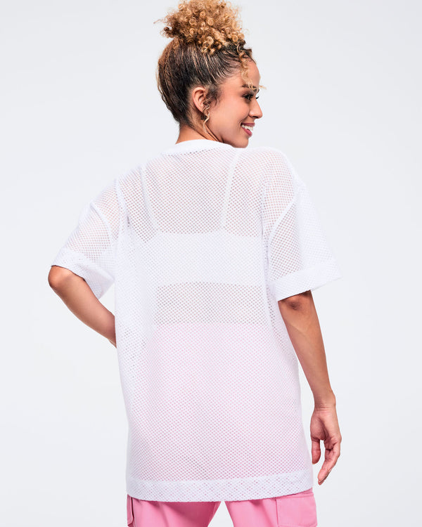 Back view of a white oversized mesh short-sleeve crewneck top with a loose, breathable see-through knit and longline hem; shown on a female model wearing pink pants.