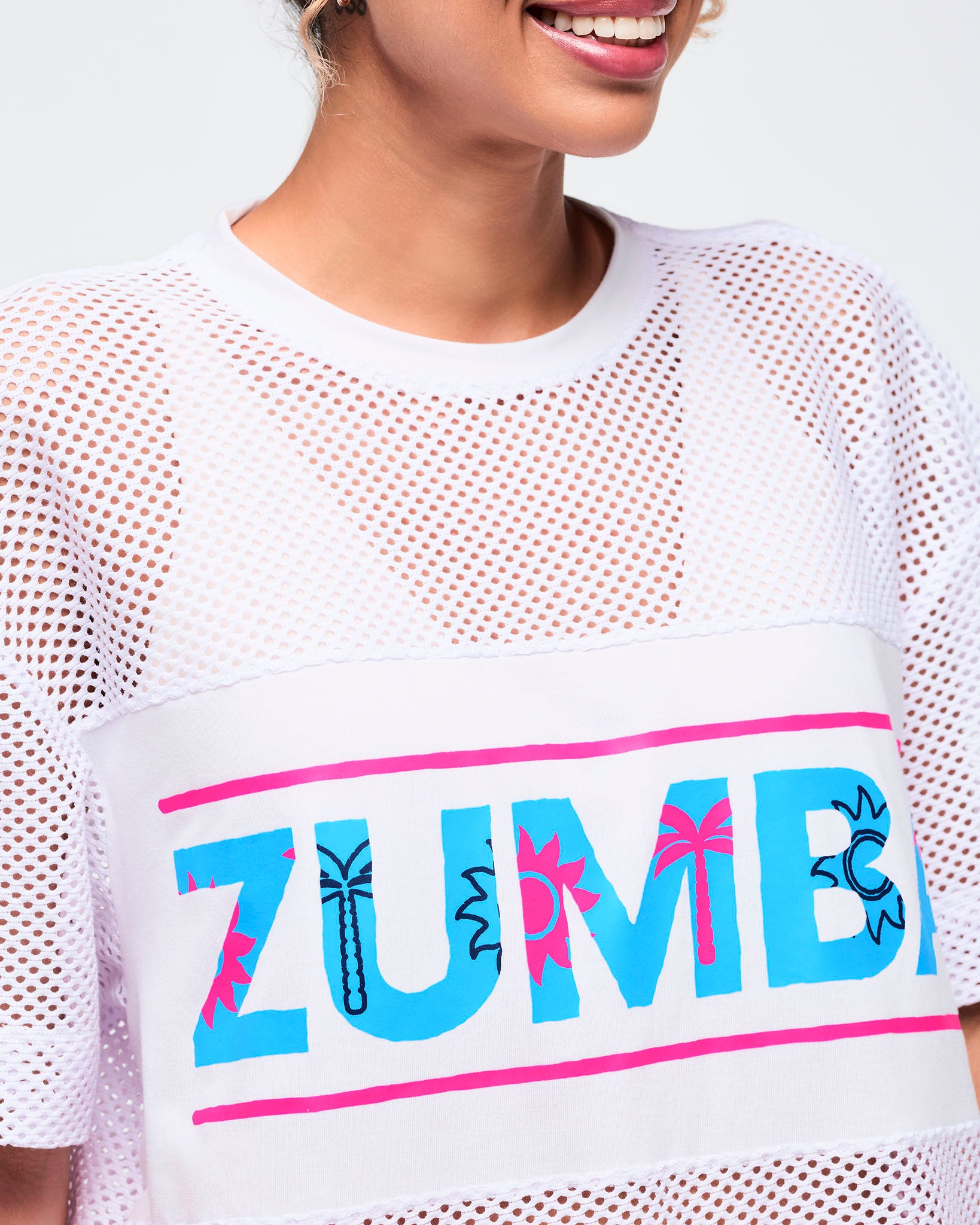 Close-up of the white crewneck top showing the mesh texture and the turquoise “ZUMBA” logo across the chest with hot-pink border details.