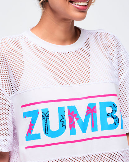 Close-up of the white crewneck top showing the mesh texture and the turquoise “ZUMBA” logo across the chest with hot-pink border details.