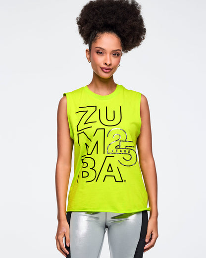 Neon green sleeveless Zumba tank with oversized black logo graphics and a silver “25 Years” detail on the front. Female model wears the relaxed-fit muscle tank with shiny metallic silver leggings featuring black side panels, shown in a front view against a light gray background.