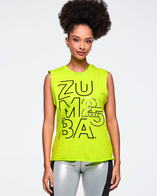 Neon green sleeveless Zumba tank with oversized black logo graphics and a silver “25 Years” detail on the front. Female model wears the relaxed-fit muscle tank with shiny metallic silver leggings featuring black side panels, shown in a front view against a light gray background.