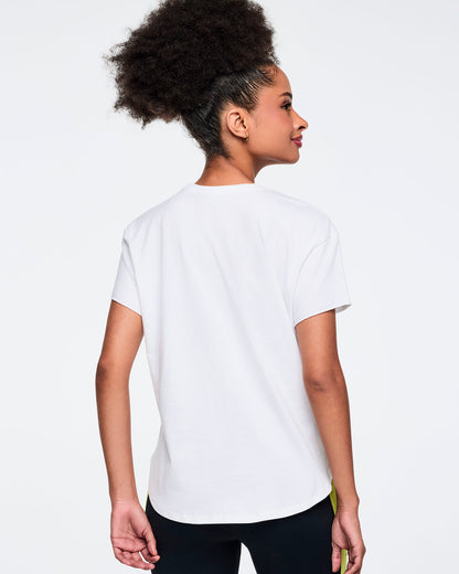 White short-sleeve Zumba graphic T-shirt with a plain solid back. Female model wears the relaxed-fit tee with black leggings featuring neon yellow side panels, shown from the back against a light gray background.