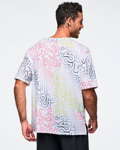 White oversized mesh Zumba top with multicolor allover logo print. Male model wears the relaxed short-sleeve top with black athletic pants, shown from the back against a light gray background.