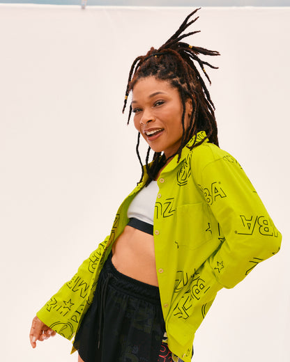 Female model wears the oversized collared shirt open over the sports bra with loose black shorts, posing in front of a white backdrop.