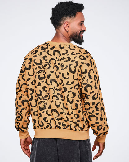 Back view of a tan crewneck sweatshirt with an allover black leopard print and ribbed cuffs, collar, and hem. Male model wears the long-sleeve sweatshirt with dark charcoal washed pants, standing turned slightly to the side and smiling against a light gray background.