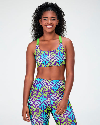 Female model in the purple and aqua warped 'ZUMBA' print scoop neck bra with neon green straps and matching high-waisted leggings.