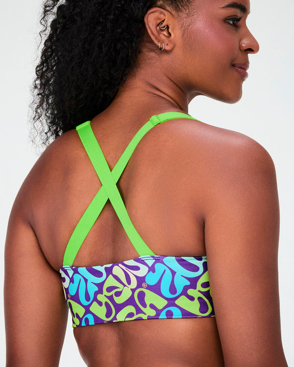 Close-up of the back of the warped 'ZUMBA' print bra, showing neon green straps crossing between the shoulder blades.