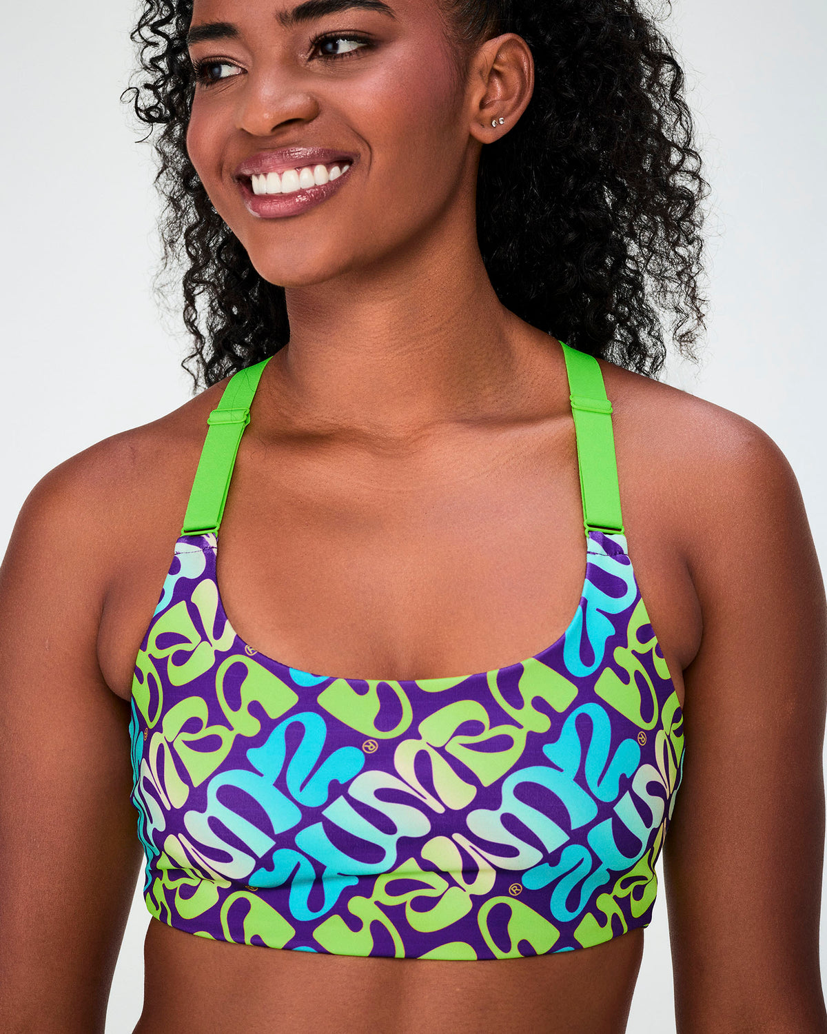 Close-up of the purple and aqua warped 'ZUMBA' print scoop neck bra, showing the wide neon green straps and scoop neckline.