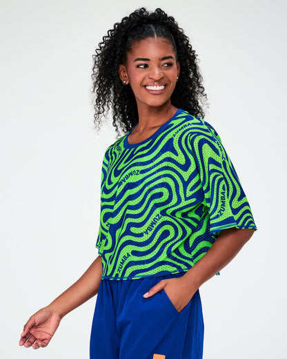 Female model in the neon green and blue wavy print mesh crop top, shown in side view with its dropped shoulders and boxy length.