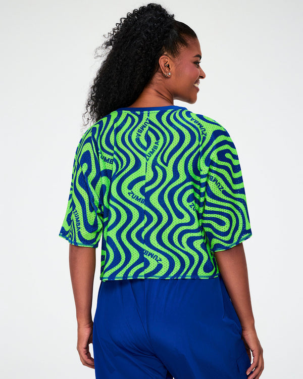 Shown from the back, the neon green and blue wavy print mesh crop top, with 'ZUMBA' text curving through the print across the back.