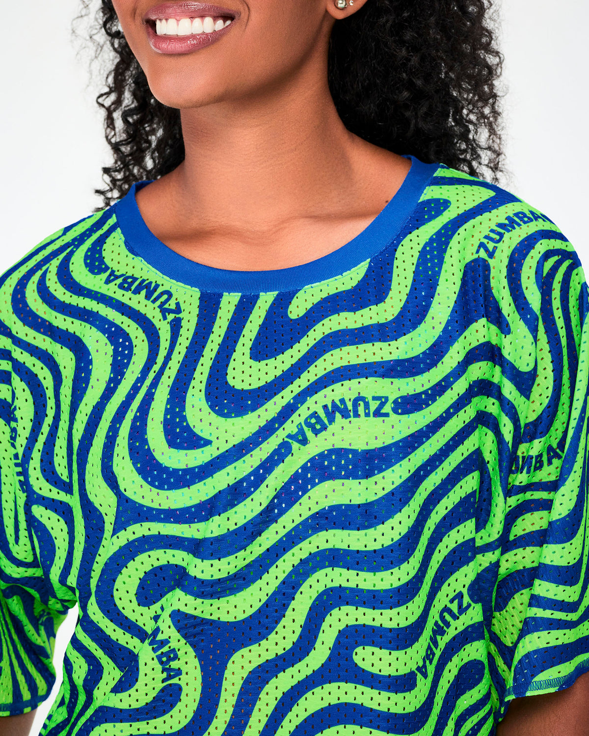 Close-up of the neon green and blue wavy print mesh crop top, showing the open-hole mesh, the blue neckband, and 'ZUMBA' text following the waves.