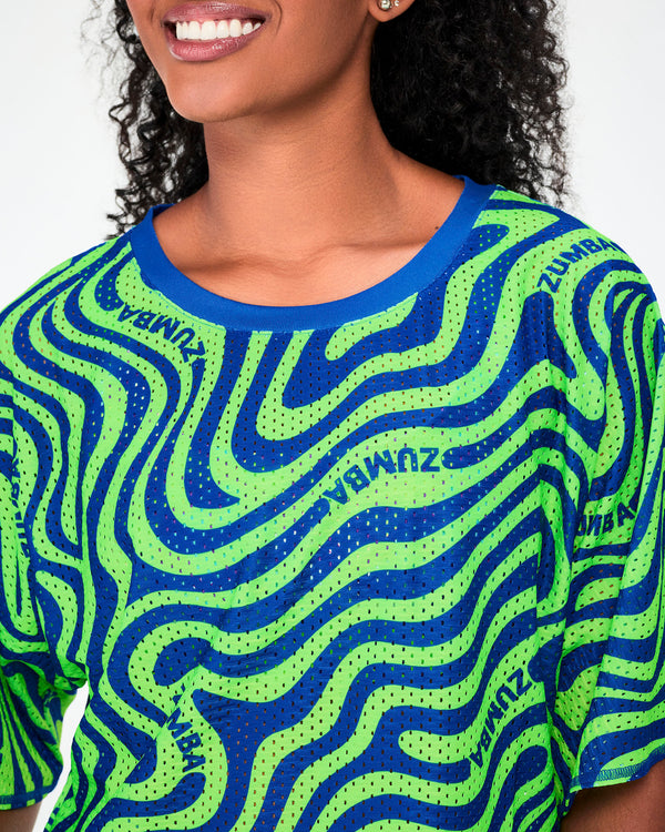 Close-up of the neon green and blue wavy print mesh crop top, showing the open-hole mesh, the blue neckband, and 'ZUMBA' text following the waves.