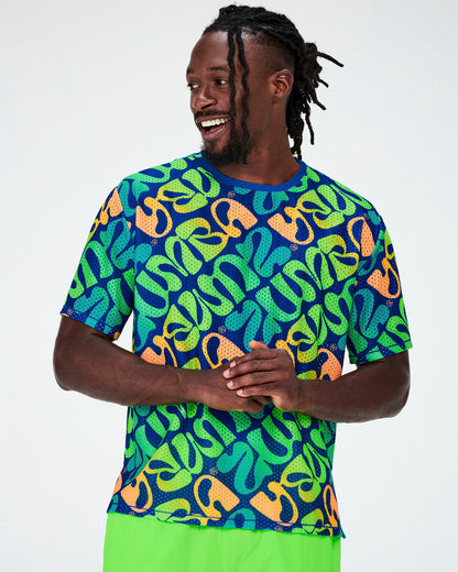 Male model in a blue mesh boxy top with an all-over diagonal print of warped 'ZUMBA' lettering in neon green, aqua, and orange, small Zumbito logos, and a blue neckband, paired with neon green pants.