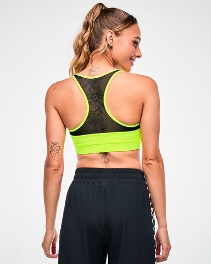 Back view of a female model in a yellow-green sports bra with a mesh racerback panel, paired with black pants.