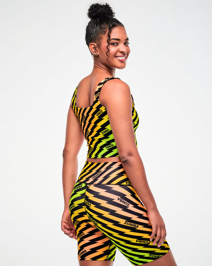 Female model wearing a yellow, green, and orange ombre crop top and matching biker shorts with a black lightning bolt zigzag print, side view.
