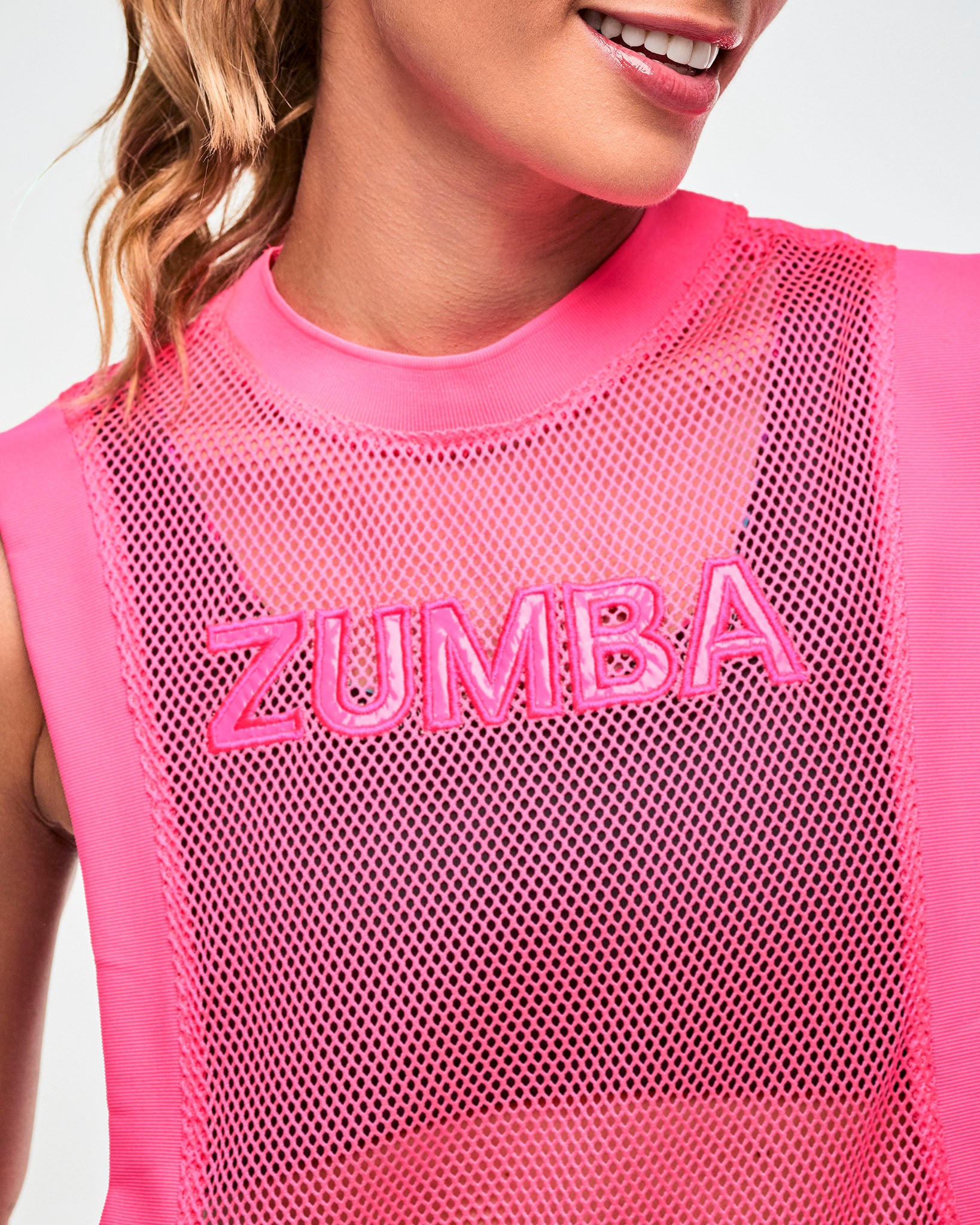 Close-up of embroidered "ZUMBA" text on a pink mesh tank.