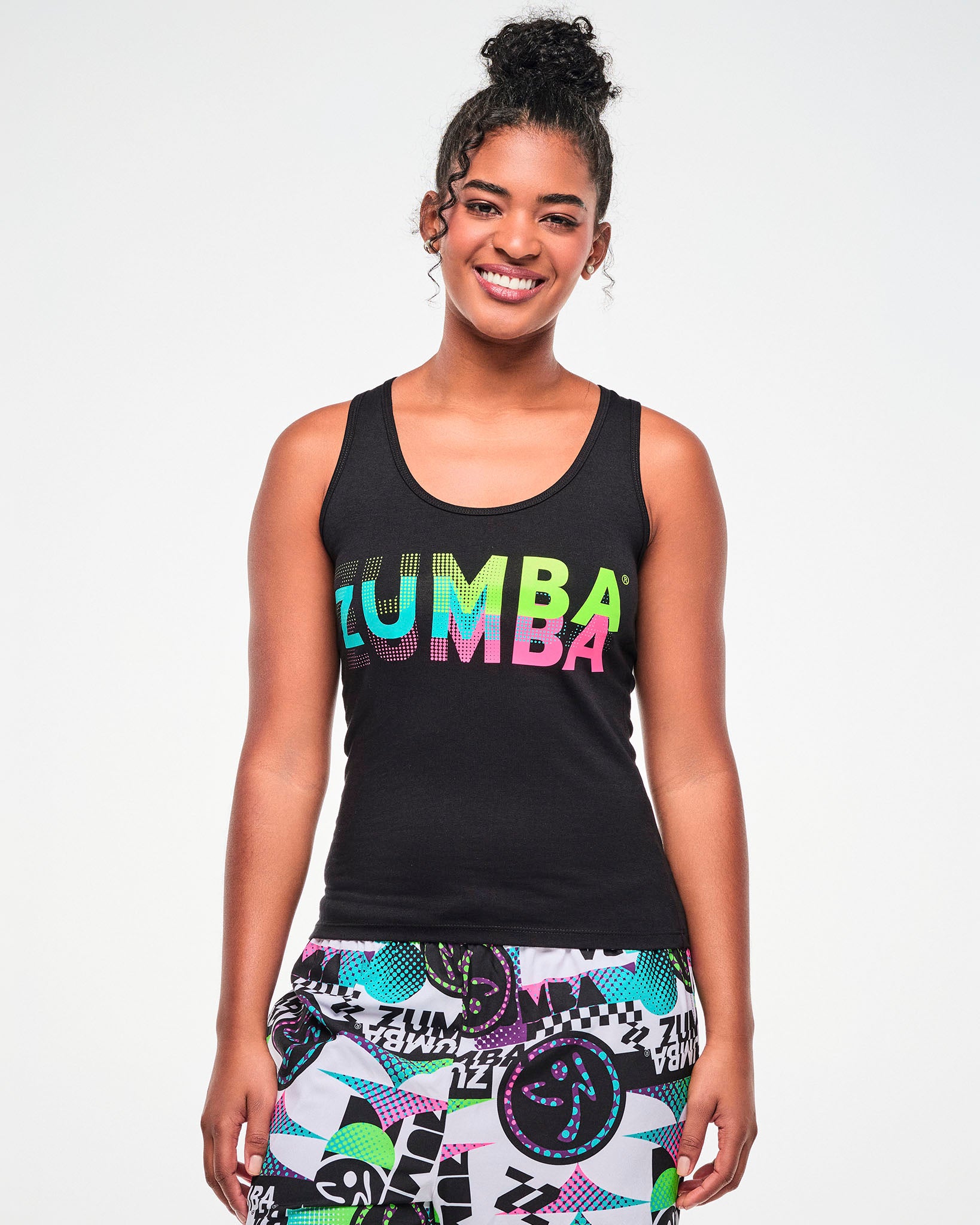 Female model wearing a black ribbed tank with blue, green and pink dots to solid print ZUMBA, paired with multicolor  pants.