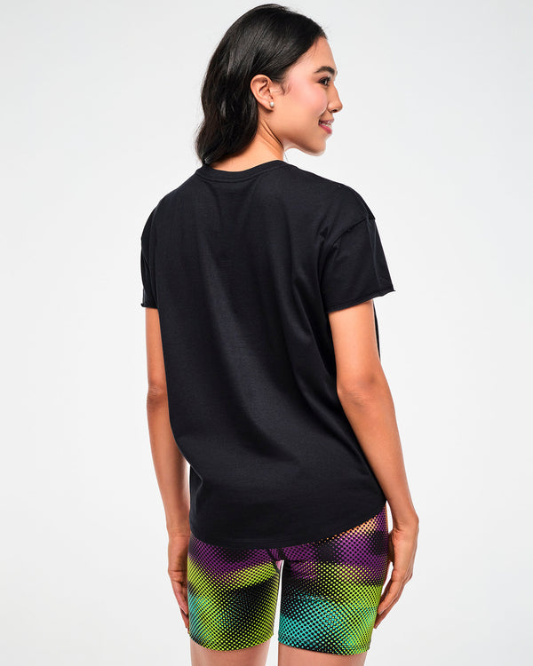 Shown from the back, female model wearing a black tee, paired with purple, green, and yellow dot pattern biker shorts.