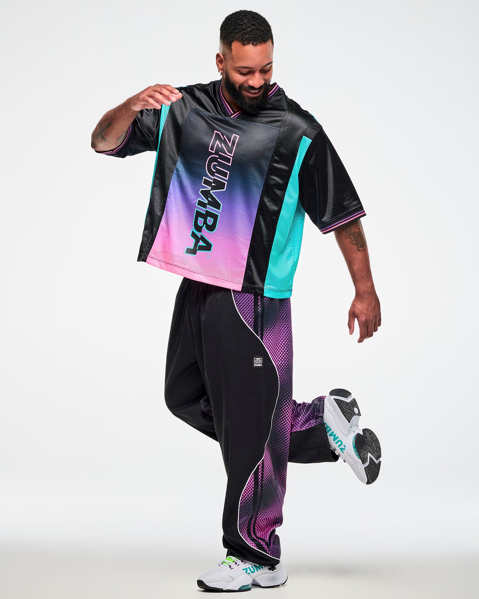 Male model wearing an oversized black jersey tee, paired with black joggers with pink side pants and white sneakers in a dynamic front pose.
